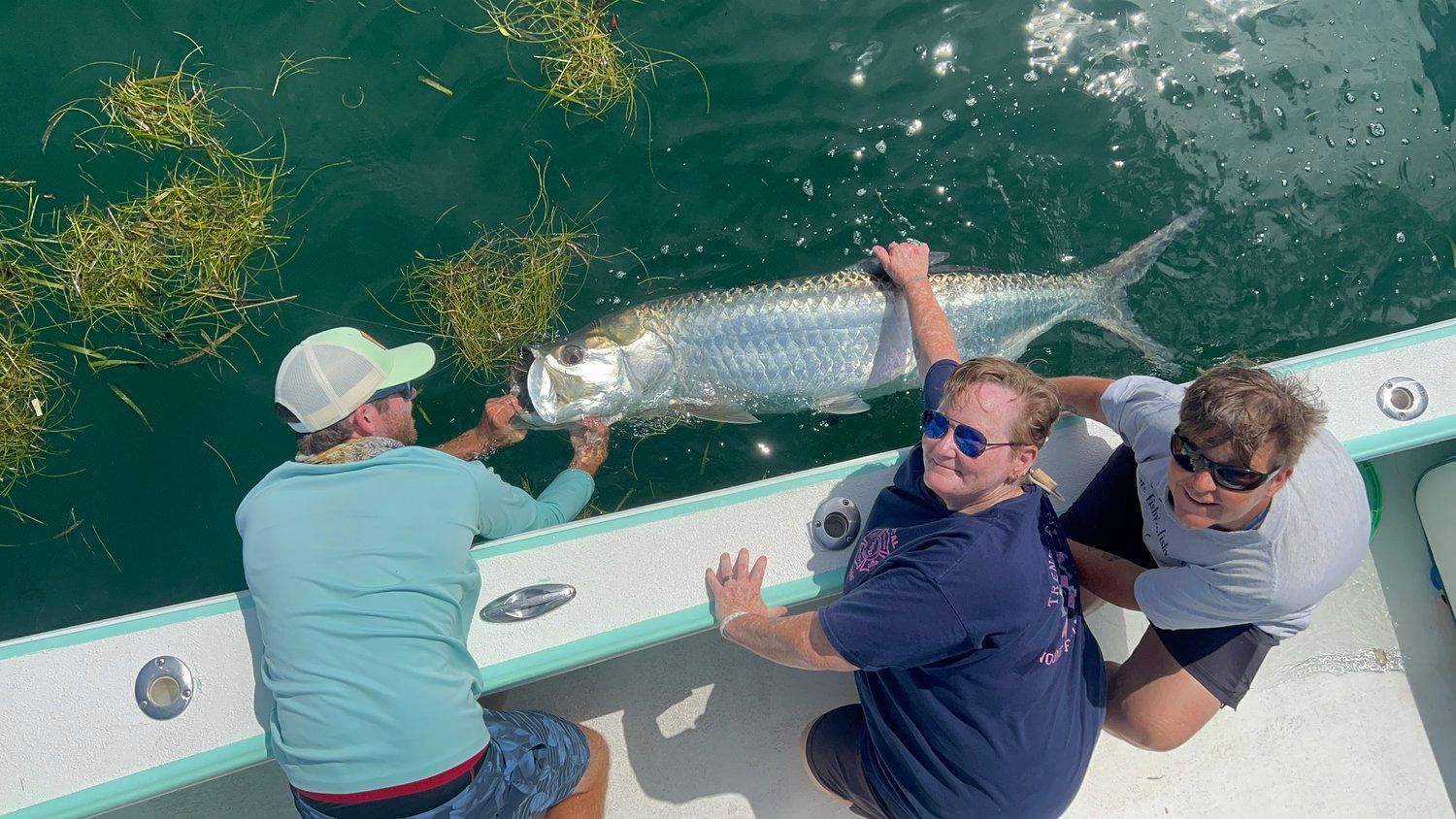 A group of people are kneeling on a boat holding a large fish.