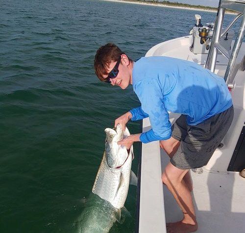 A man is holding a large fish on the side of a boat.