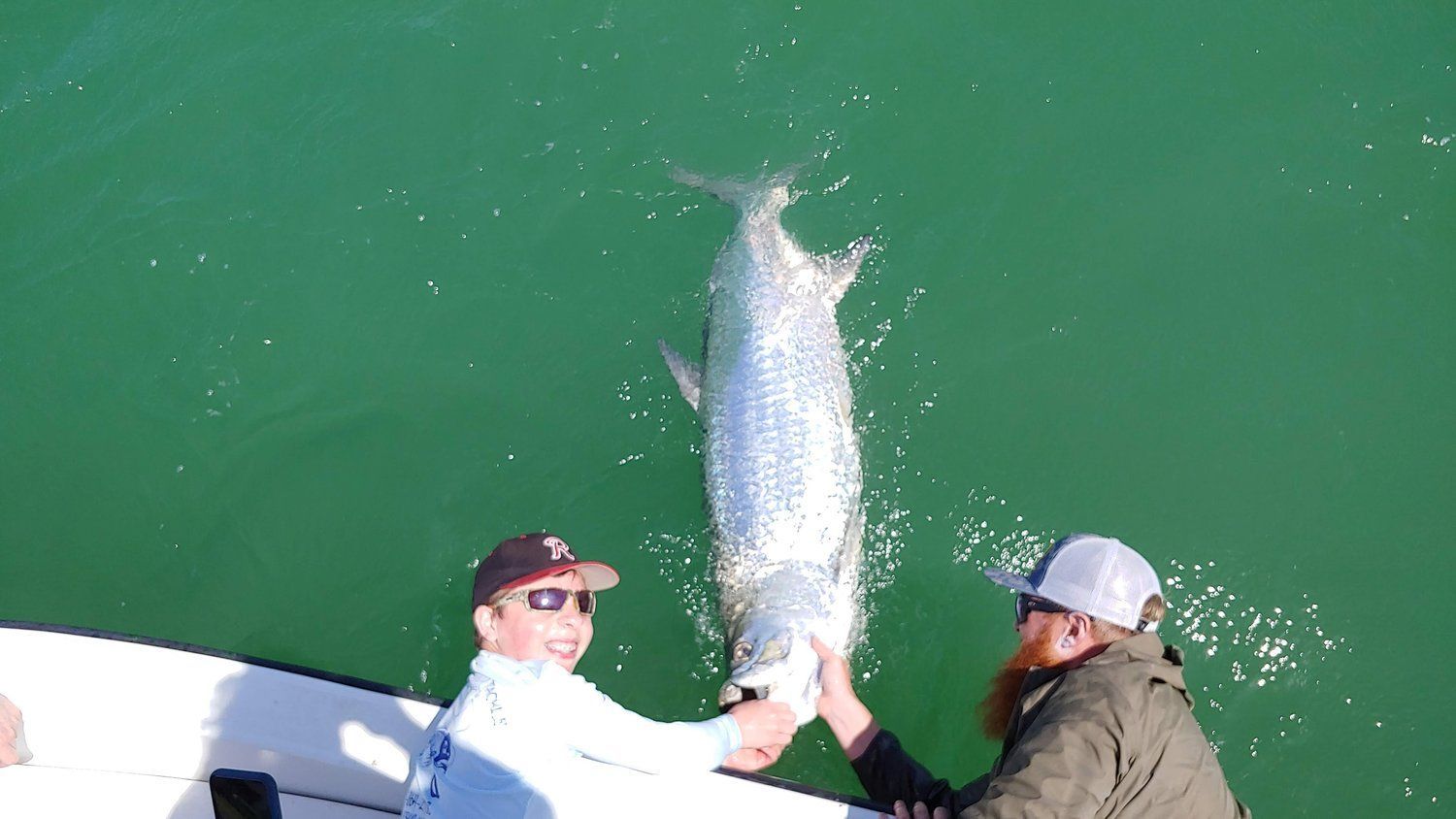 Two men are holding a large fish in the water.