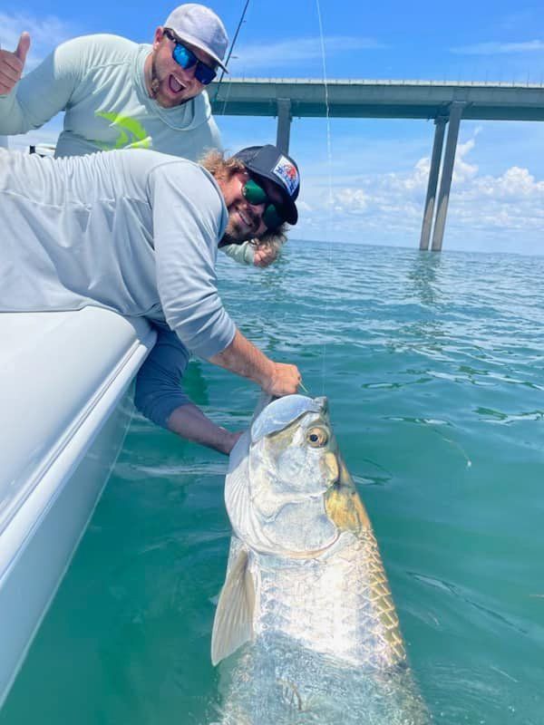 Two men are standing next to a large fish in the water.