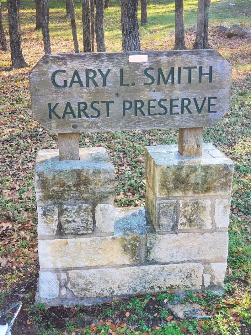 A sign for gary l. smith karst preserve is sitting on top of a stone pillar.
