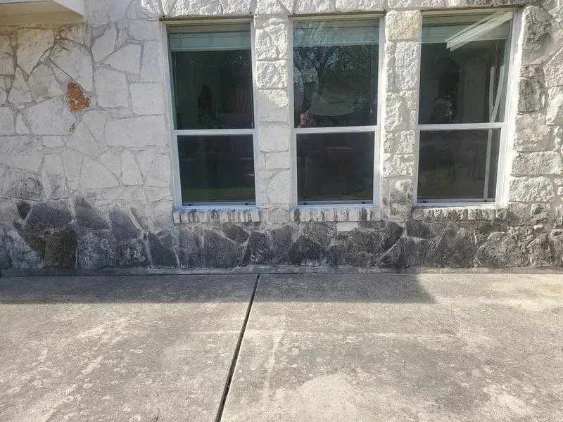 A stone building with three windows and a concrete driveway in front of it.