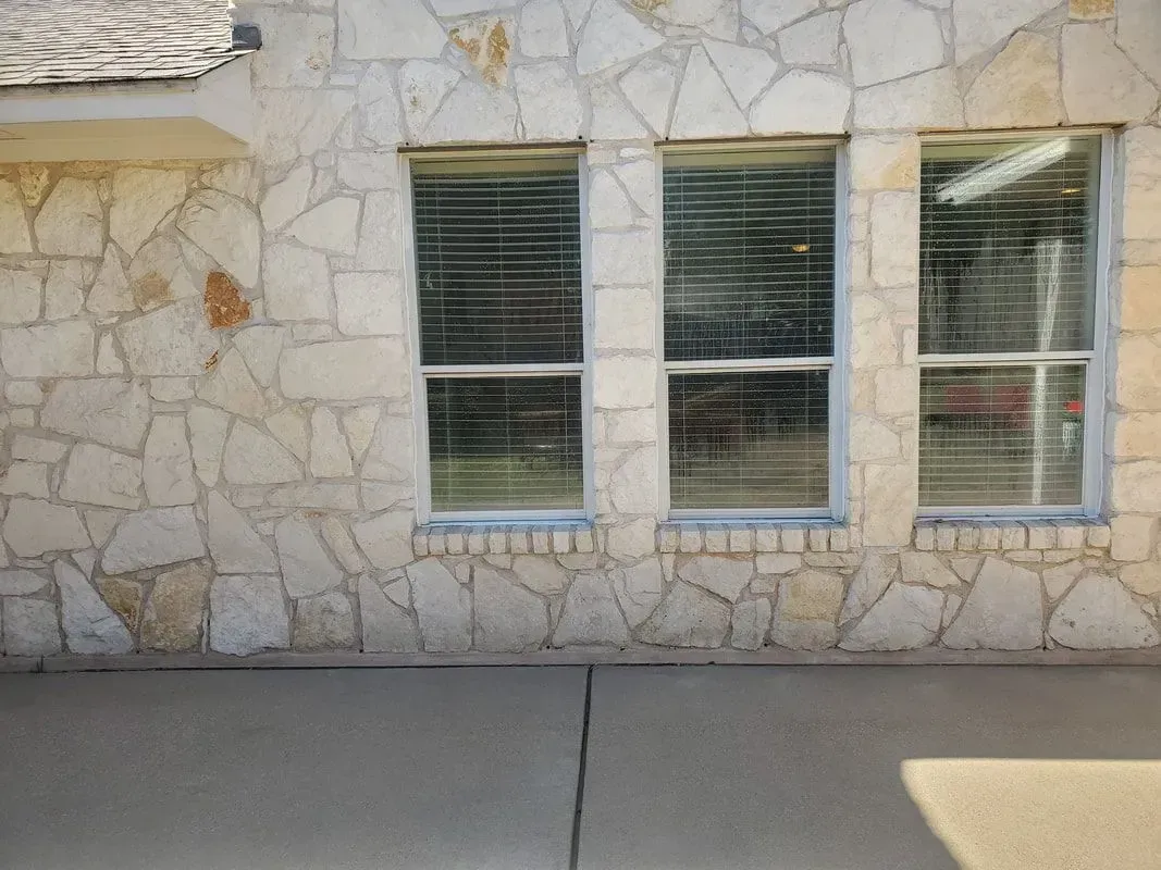 A stone wall with two windows and blinds on it