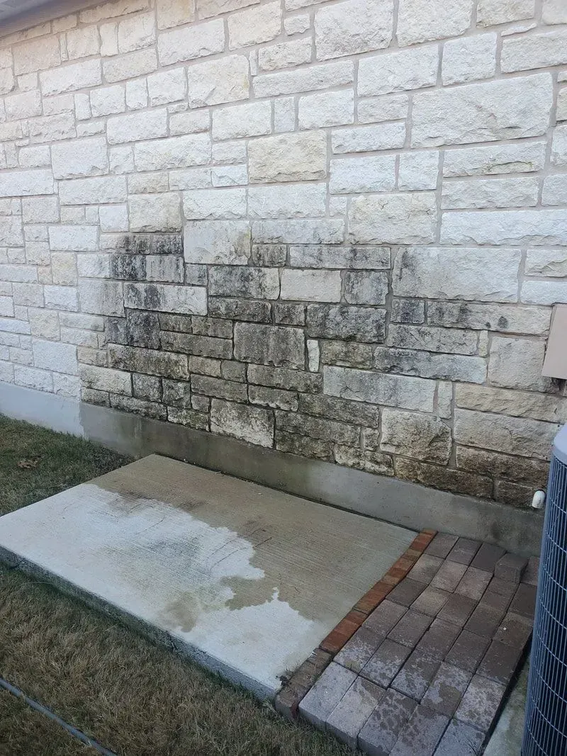 A brick wall with a concrete walkway next to it.
