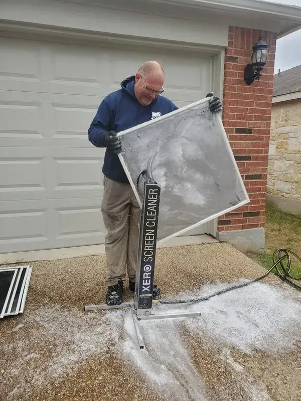 A man is cleaning a screen door in front of a garage.