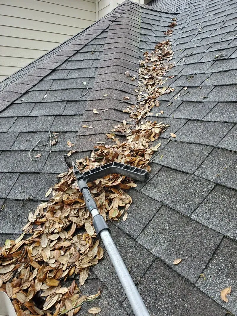 A rake is being used to remove leaves from a gutter on a roof.