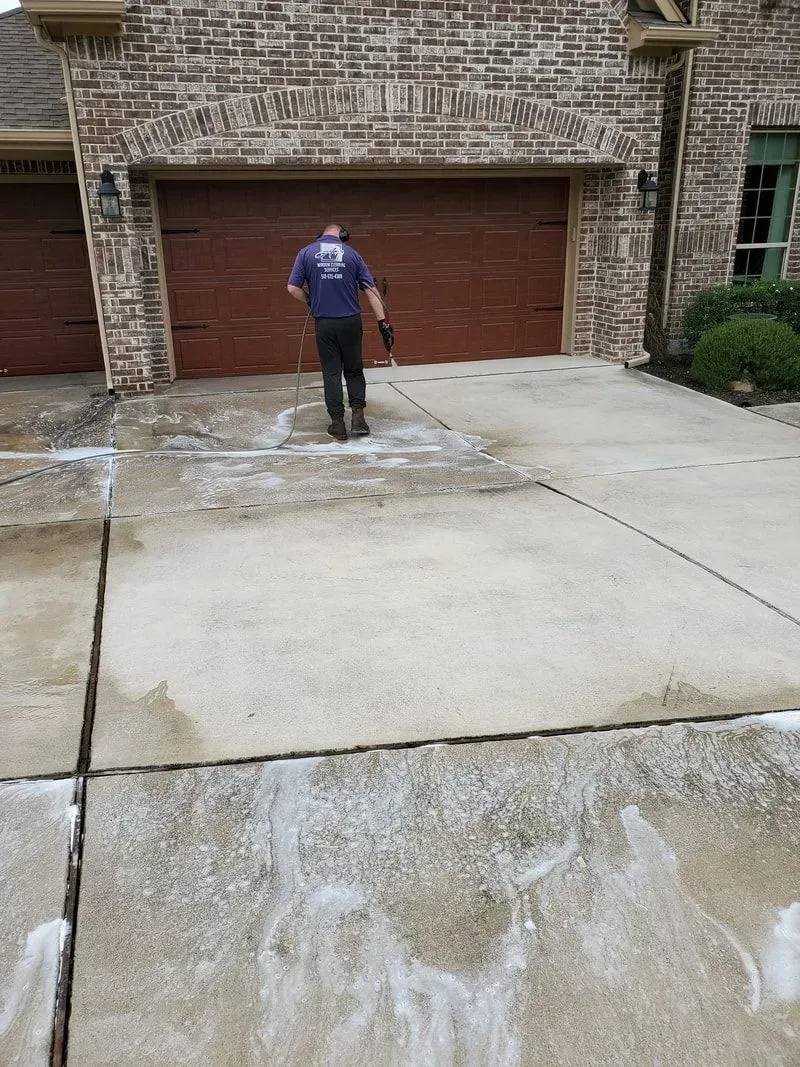 A man is cleaning the driveway of a house with a pressure washer.