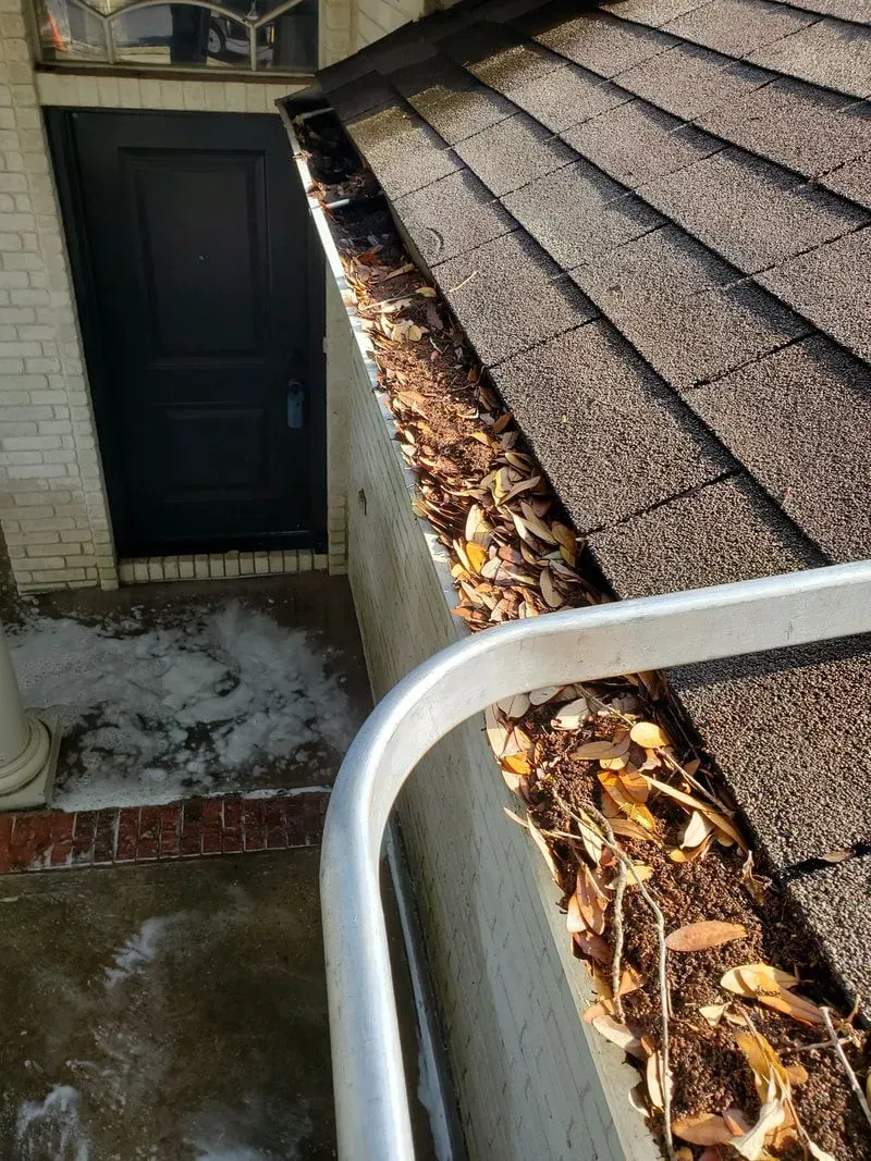 A gutter with leaves on it is on the roof of a house.