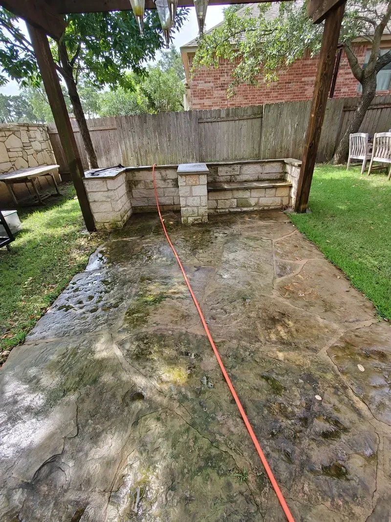 A dirty concrete patio with a hose attached to it in a backyard.