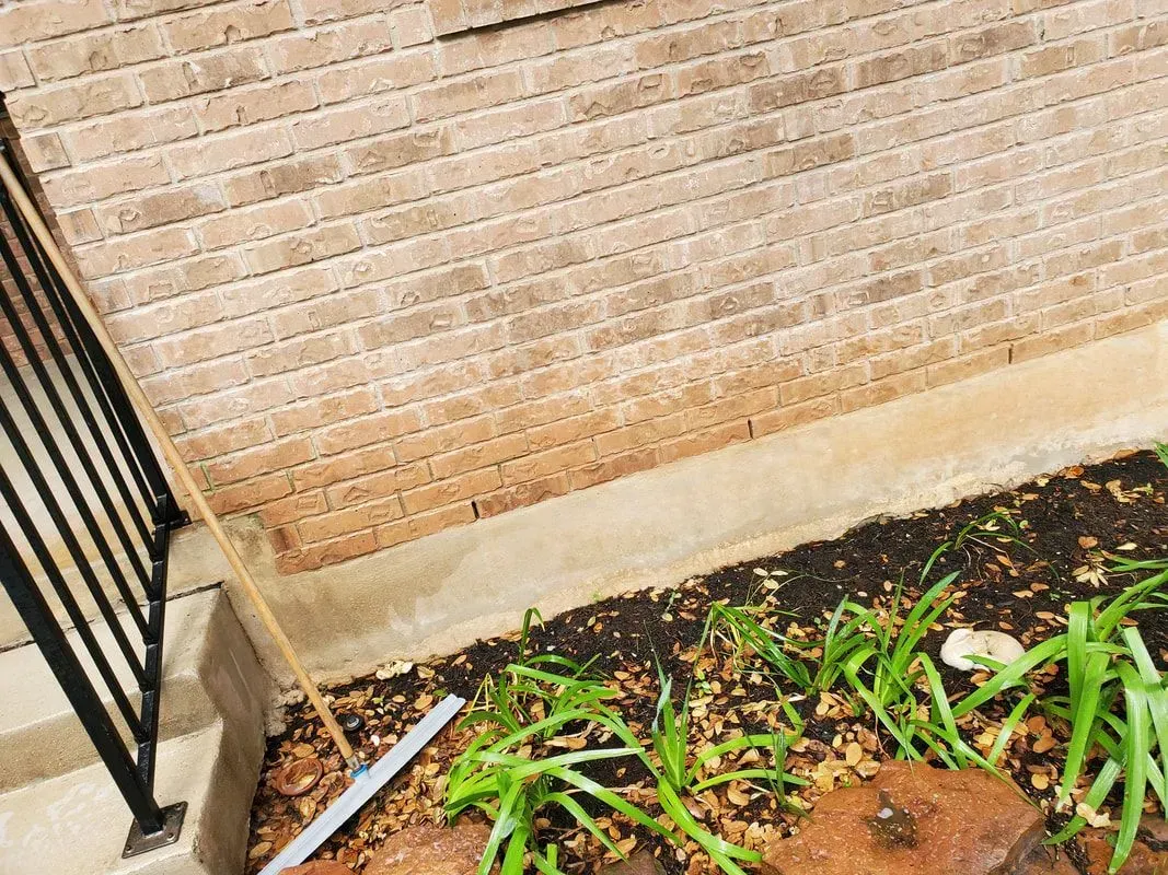 A rake is sitting in a garden next to a brick wall.