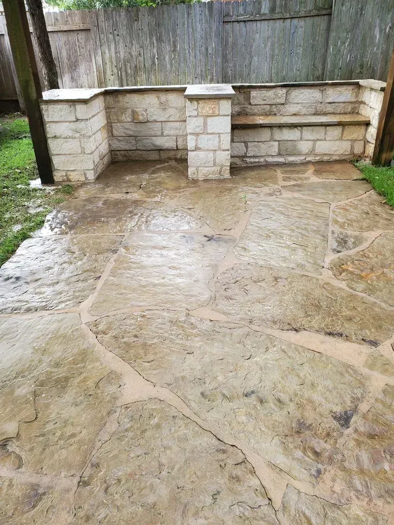 A patio with a stone wall and a bench in the backyard.