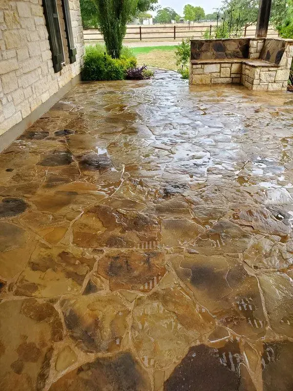 A stone patio with a brick wall and a fence in the background.