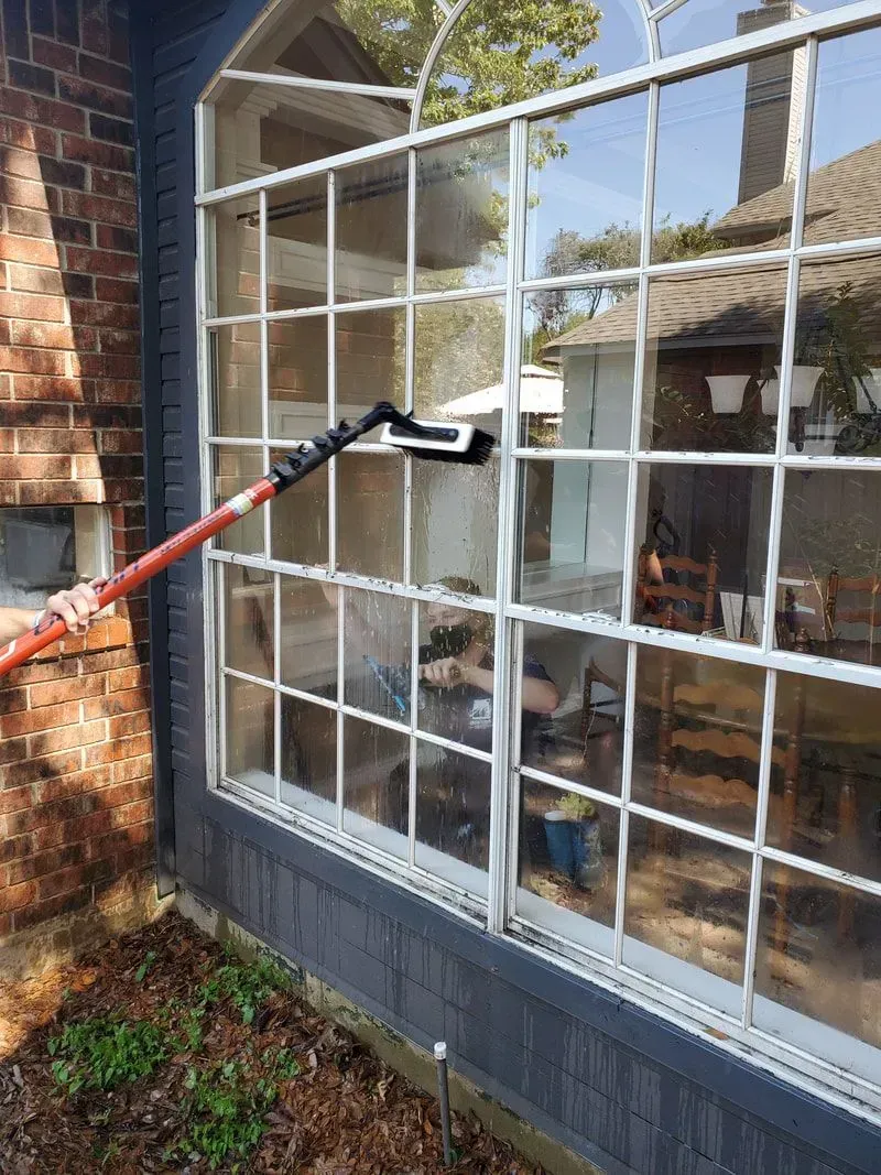A person is cleaning a window with a long pole.