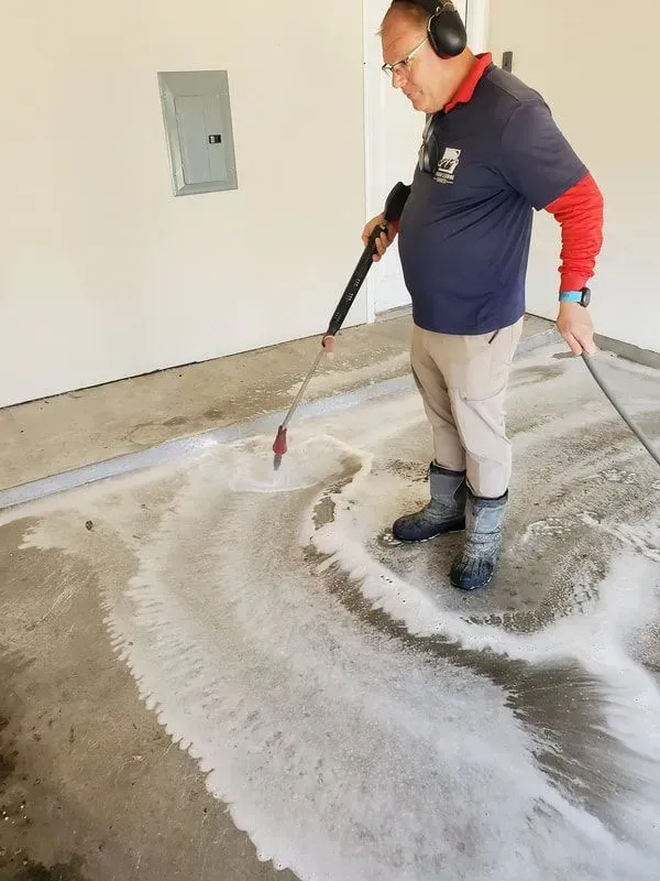 A man is using a high pressure washer to clean a concrete floor.