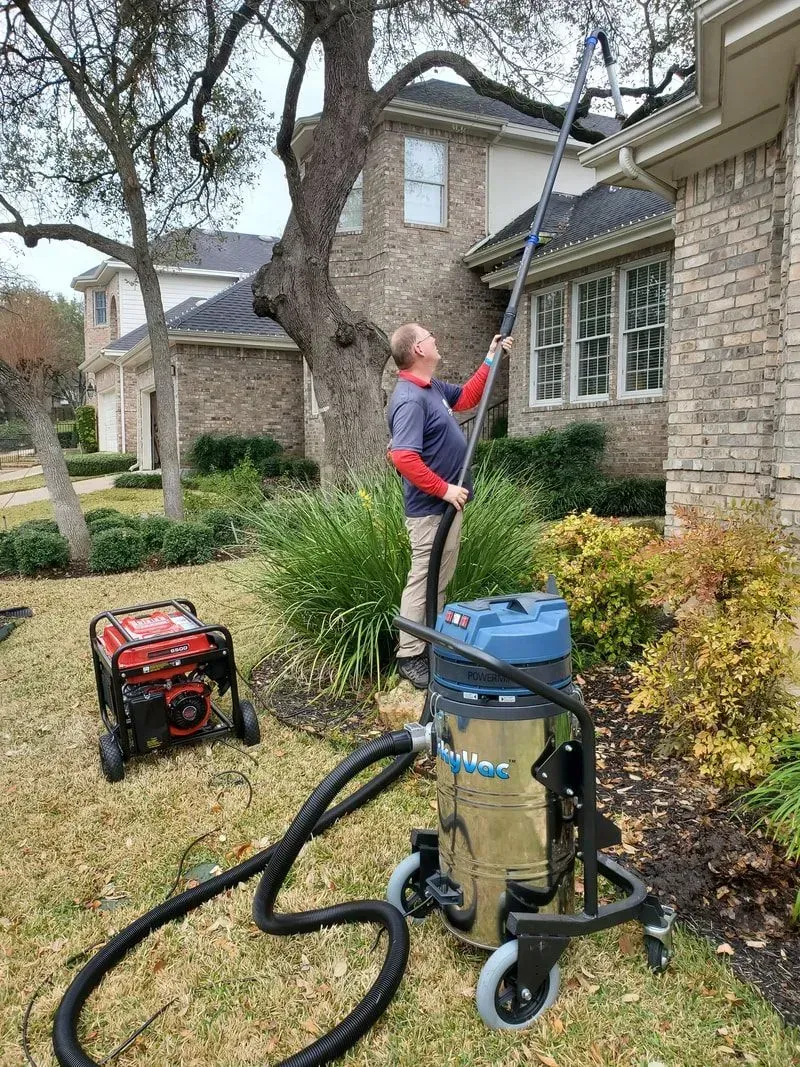 A man is using a vacuum cleaner to clean the gutters of a house.