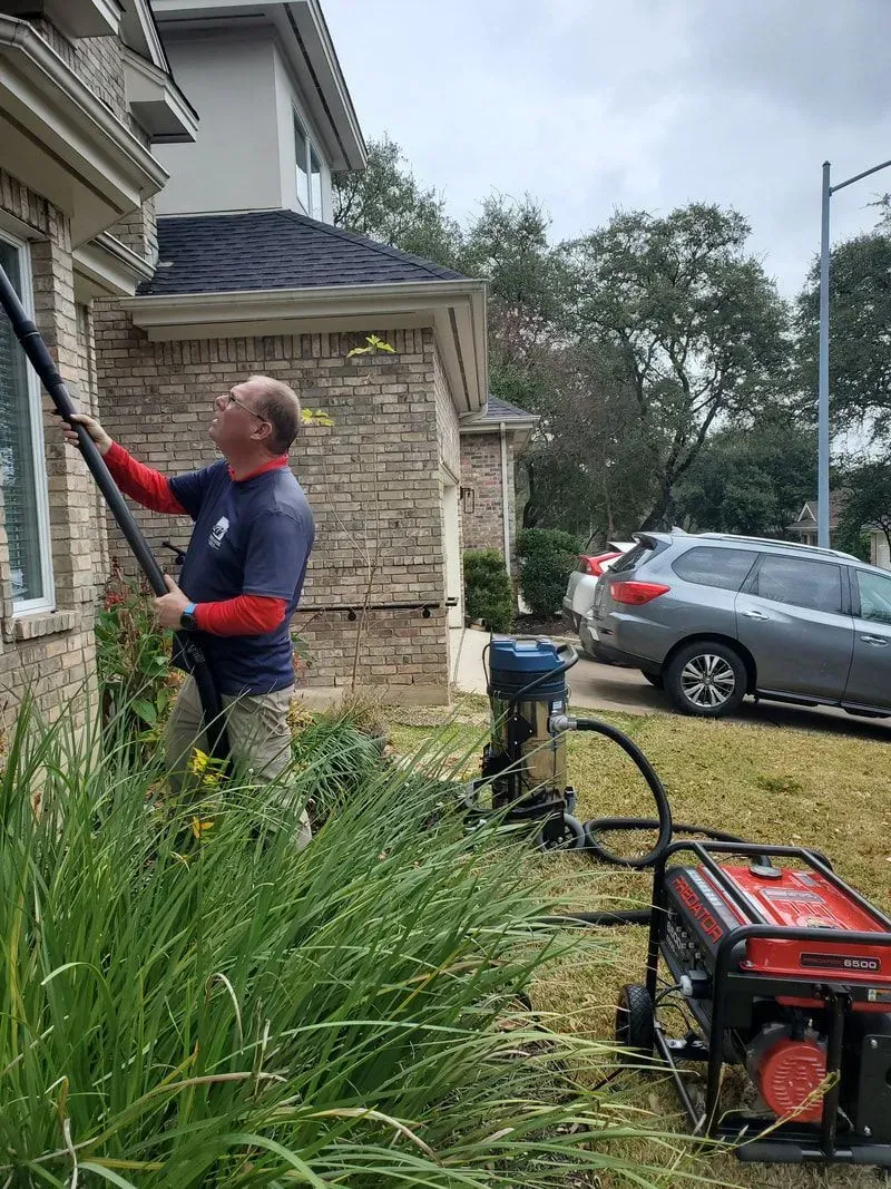 A man is cleaning the side of a house with a vacuum cleaner.