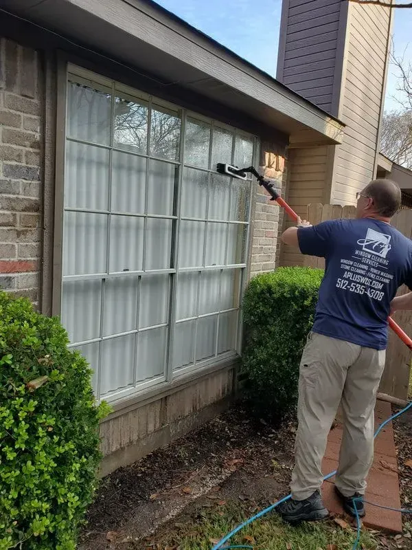 A man is cleaning a window with a hose.