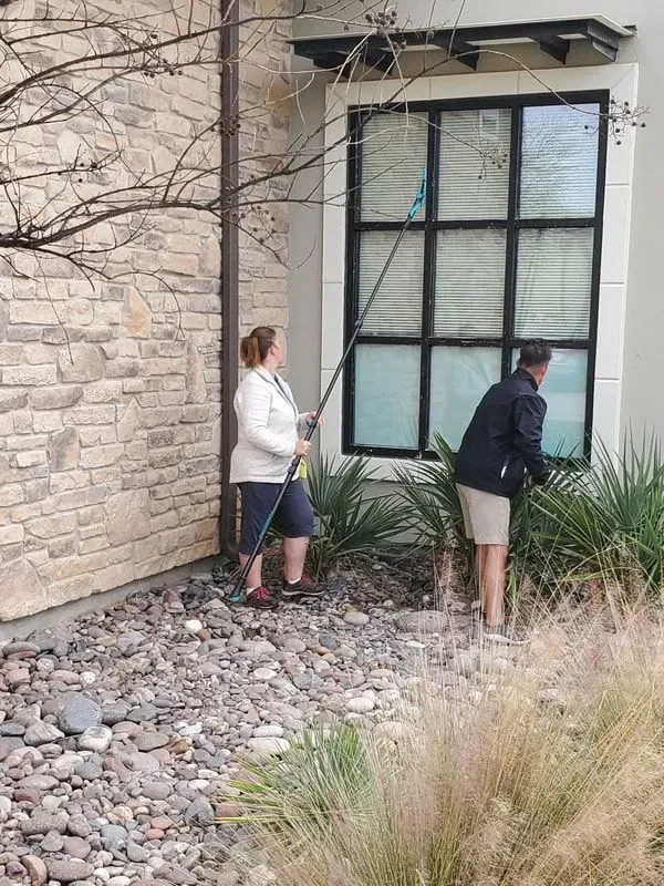 A man and a woman are cleaning a window outside of a building.