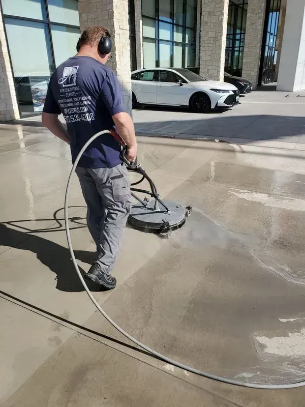 A man is cleaning a concrete driveway with a machine.