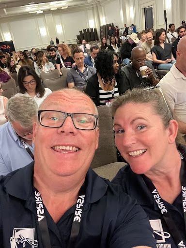 A man and a woman are taking a selfie in front of a crowd of people.