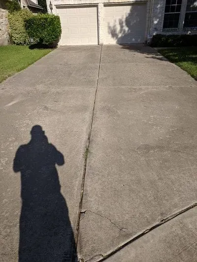 A shadow of a person is cast on a concrete driveway in front of a house.