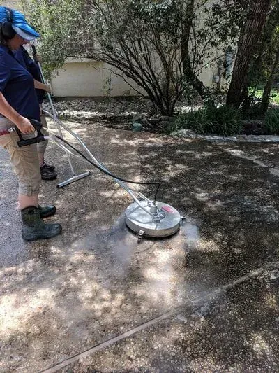 A man is using a pressure washer to clean a concrete driveway.