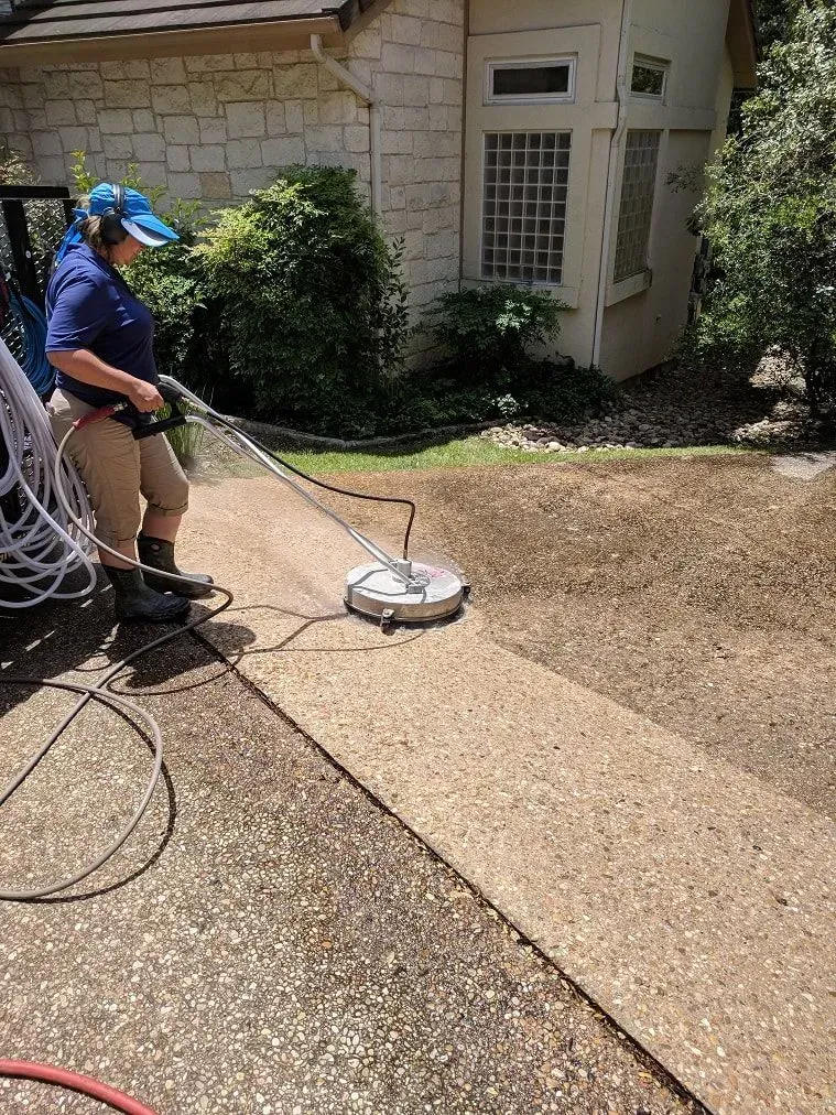A woman is cleaning a driveway with a machine.