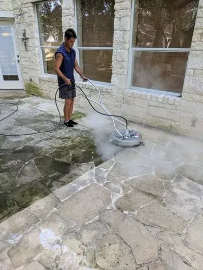 A man is cleaning a stone patio with a machine.
