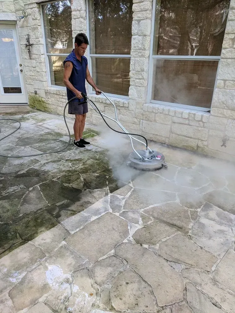 A man is cleaning a stone patio with a pressure washer.