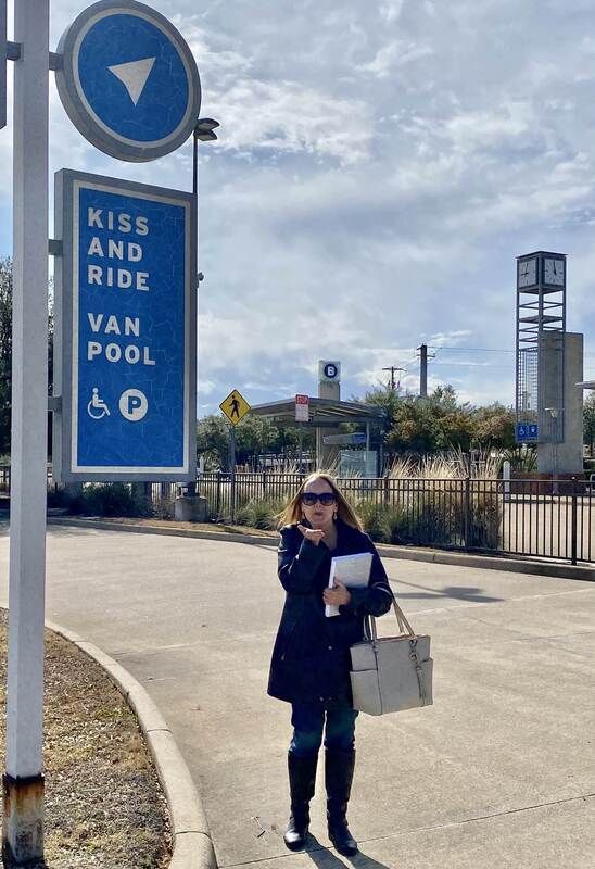 A woman blowing a kiss standing next to the kiss and ride, van pool sign