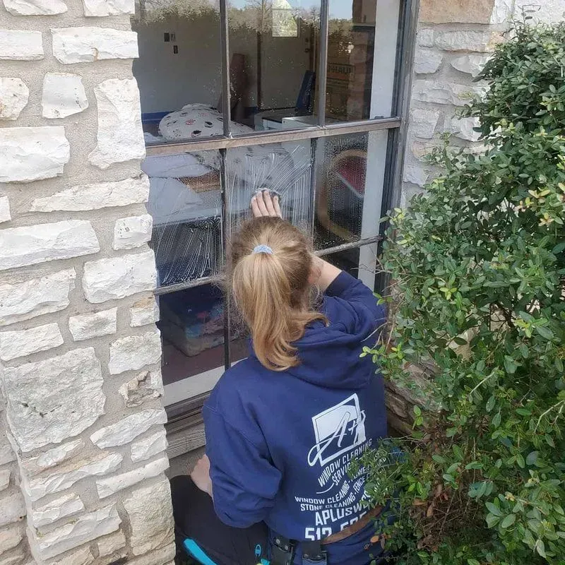 A woman in a blue hoodie is cleaning a window