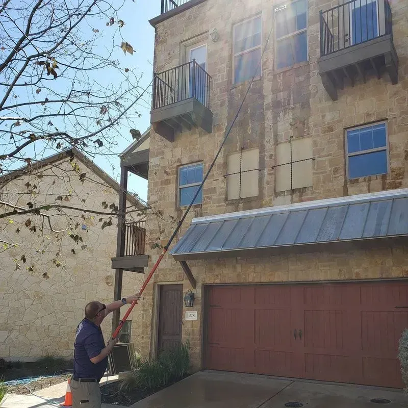 A man is cleaning a building with a long pole