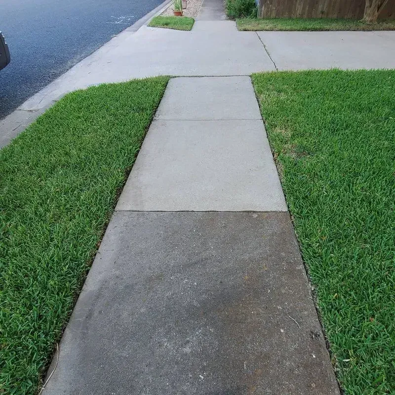 A concrete sidewalk with grass on the side of it