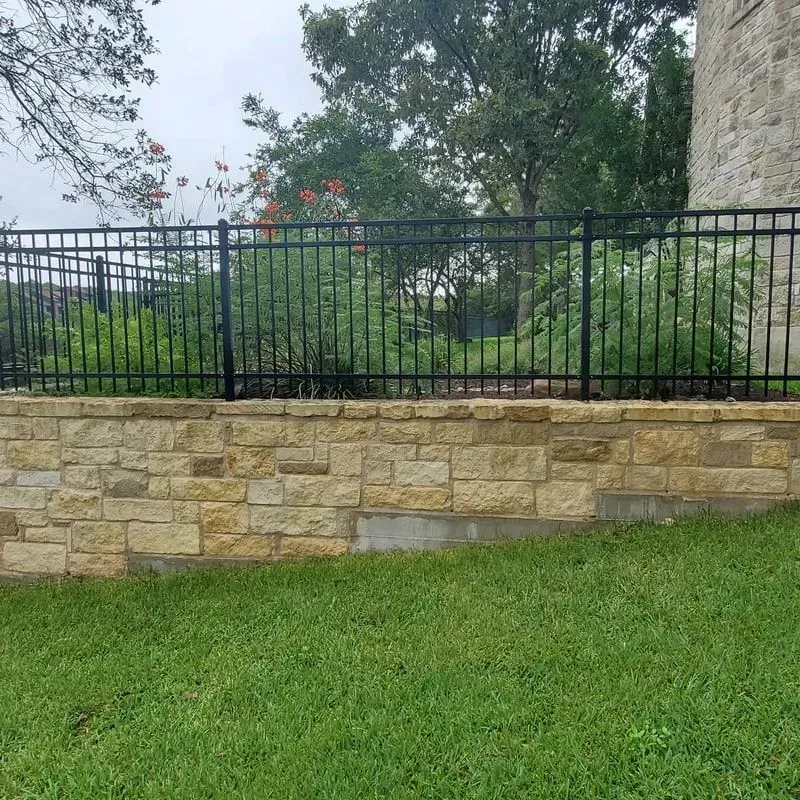A stone wall with a metal fence surrounding it.