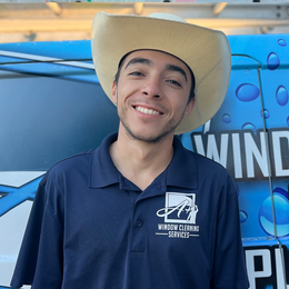 A man wearing a cowboy hat is smiling in front of a wind cleaning sign