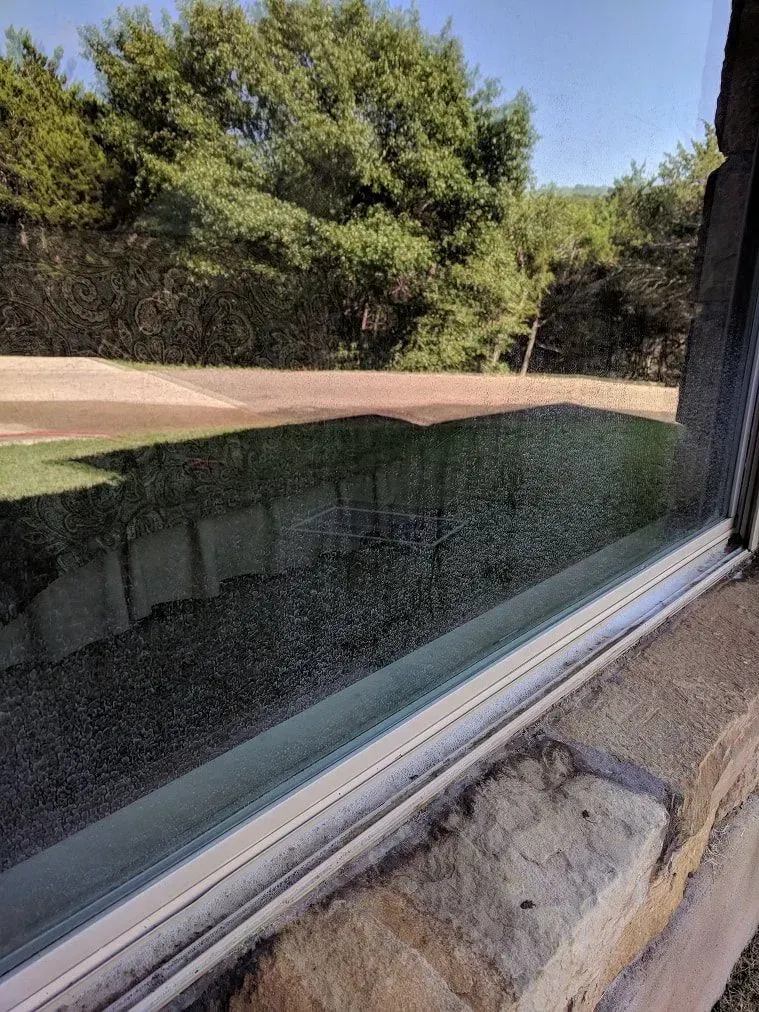 A close up of a window with a view of a field and trees.