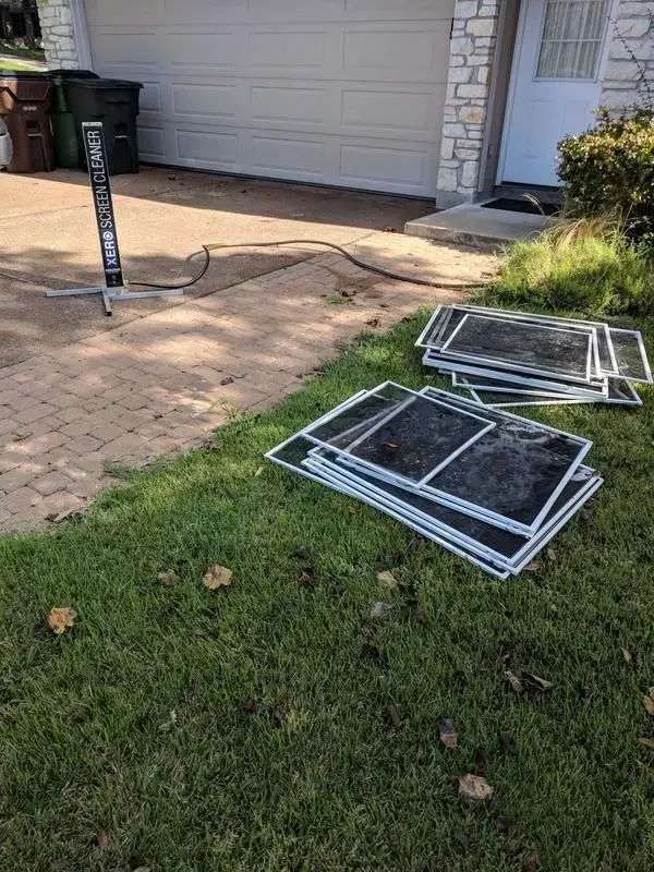 A bunch of screens are laying on the grass in front of a garage door.