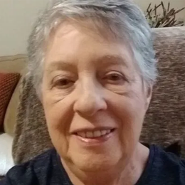 An older woman is smiling for the camera while sitting on a couch.