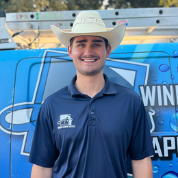 A man wearing a cowboy hat is standing in front of a blue van.