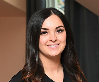 A woman with long dark hair is smiling for the camera while wearing a black scrub top.