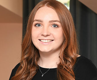 A woman with red hair is wearing a black shirt and a necklace and smiling.