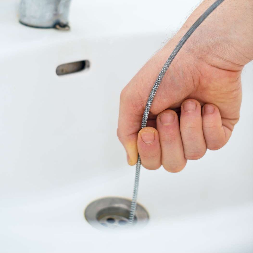 A person is holding a drain cleaner over a sink drain.