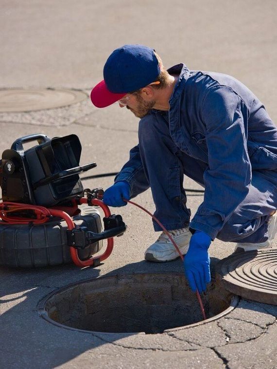 A man is looking into a manhole with a camera.