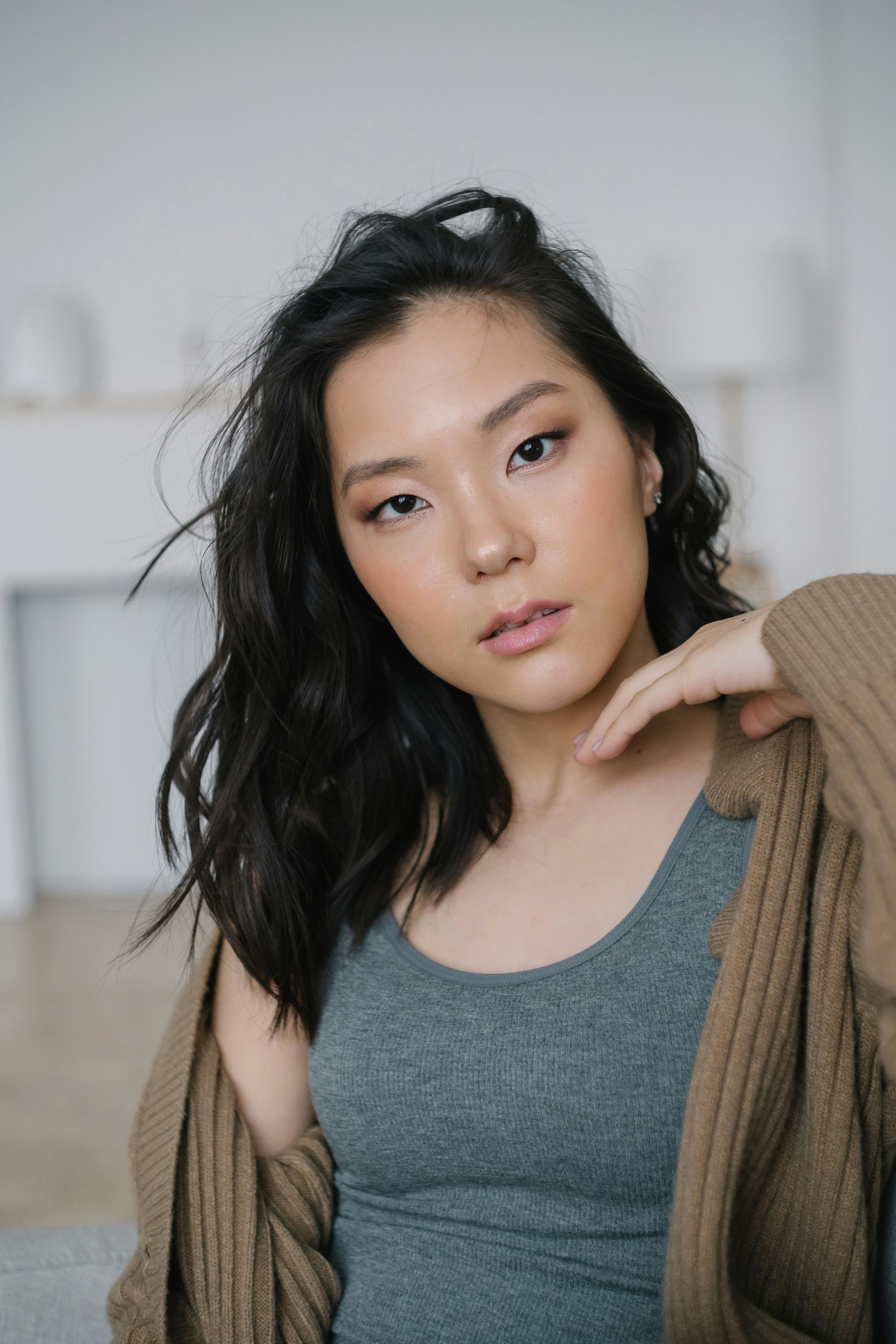 Woman with dark hair in grey tank top and brown cardigan, looking at the camera.