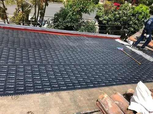 Techo negro en construcción con trabajadores, herramientas y árboles al fondo.