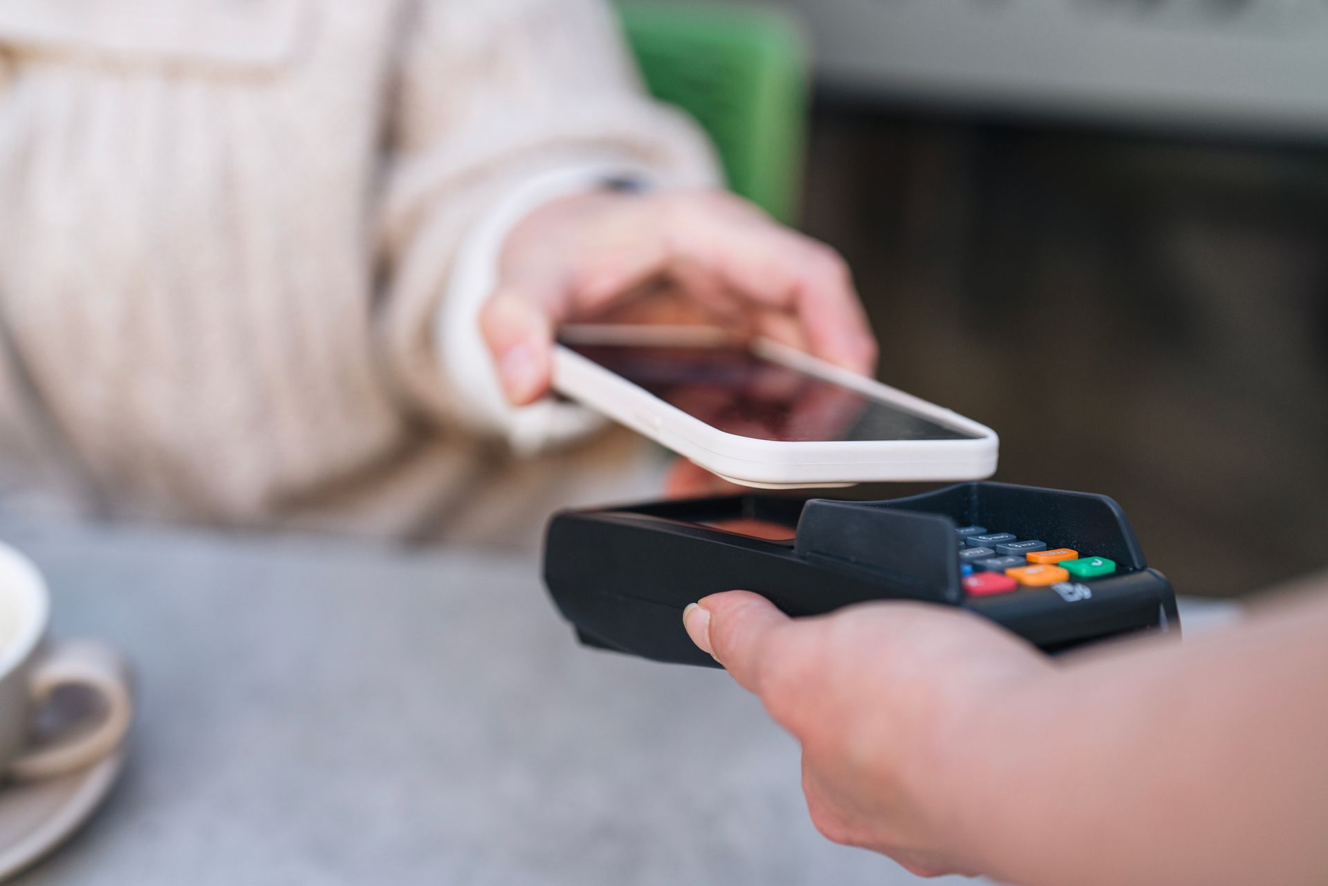 Person paying with phone held over a point-of-sale terminal.