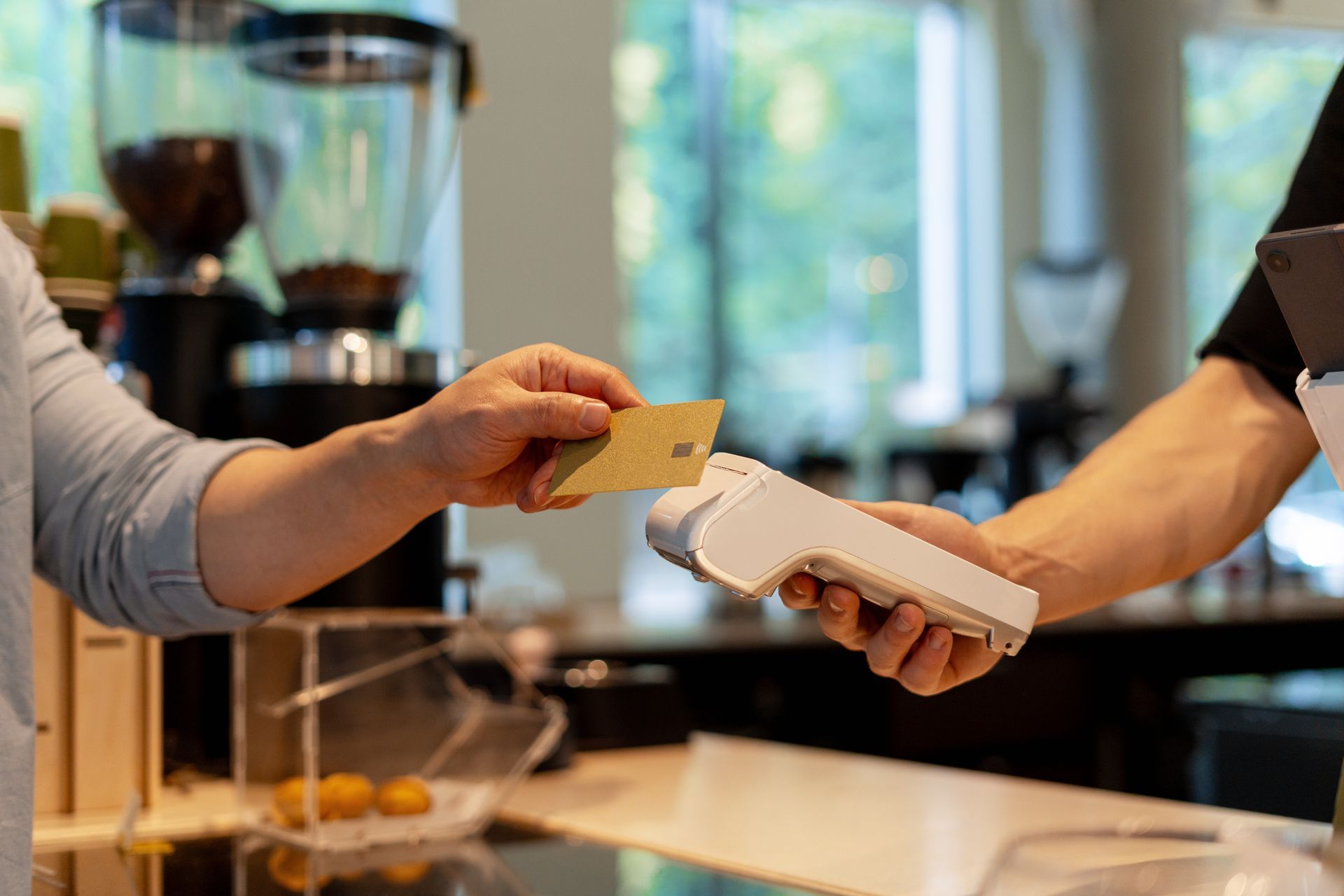 Person paying with a card at a cafe counter, tapping the card on a card reader.