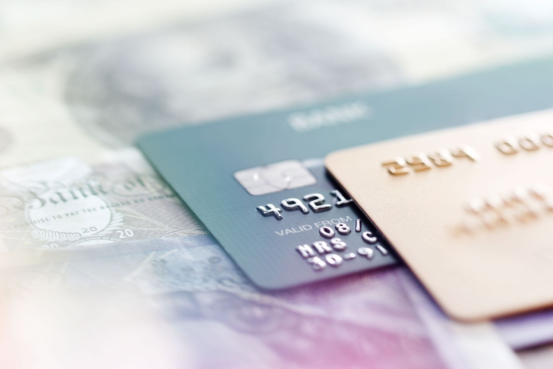 Two credit cards, teal and gold, on a blurred background of currency.