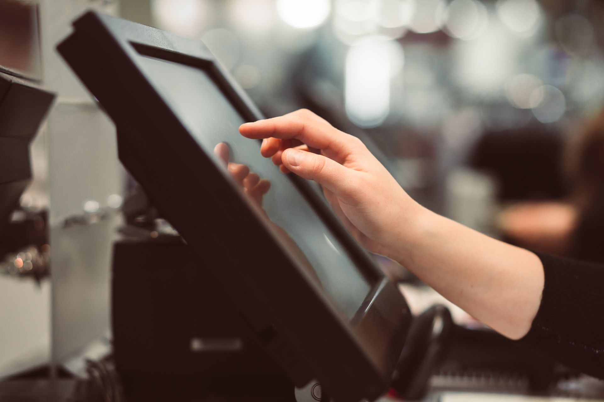 A hand touches a touchscreen point-of-sale system in a retail setting.