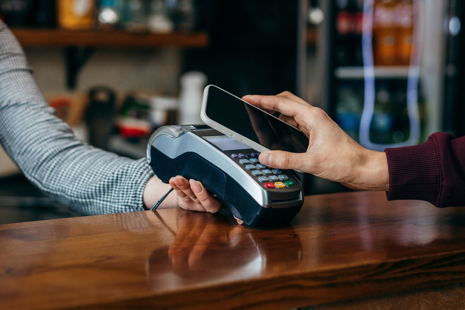 Person using smartphone to pay at a point-of-sale terminal on a wooden counter.